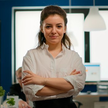 Professional woman in a white shirt standing with arms crossed in an office setting