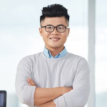 Smiling young professional man with glasses and arms crossed, standing in a bright office