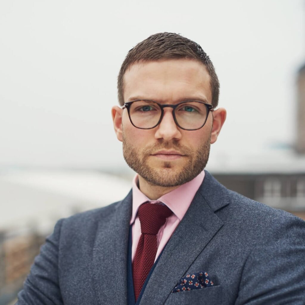 Professional man in a suit, pink shirt, and tie, looking directly at the camera